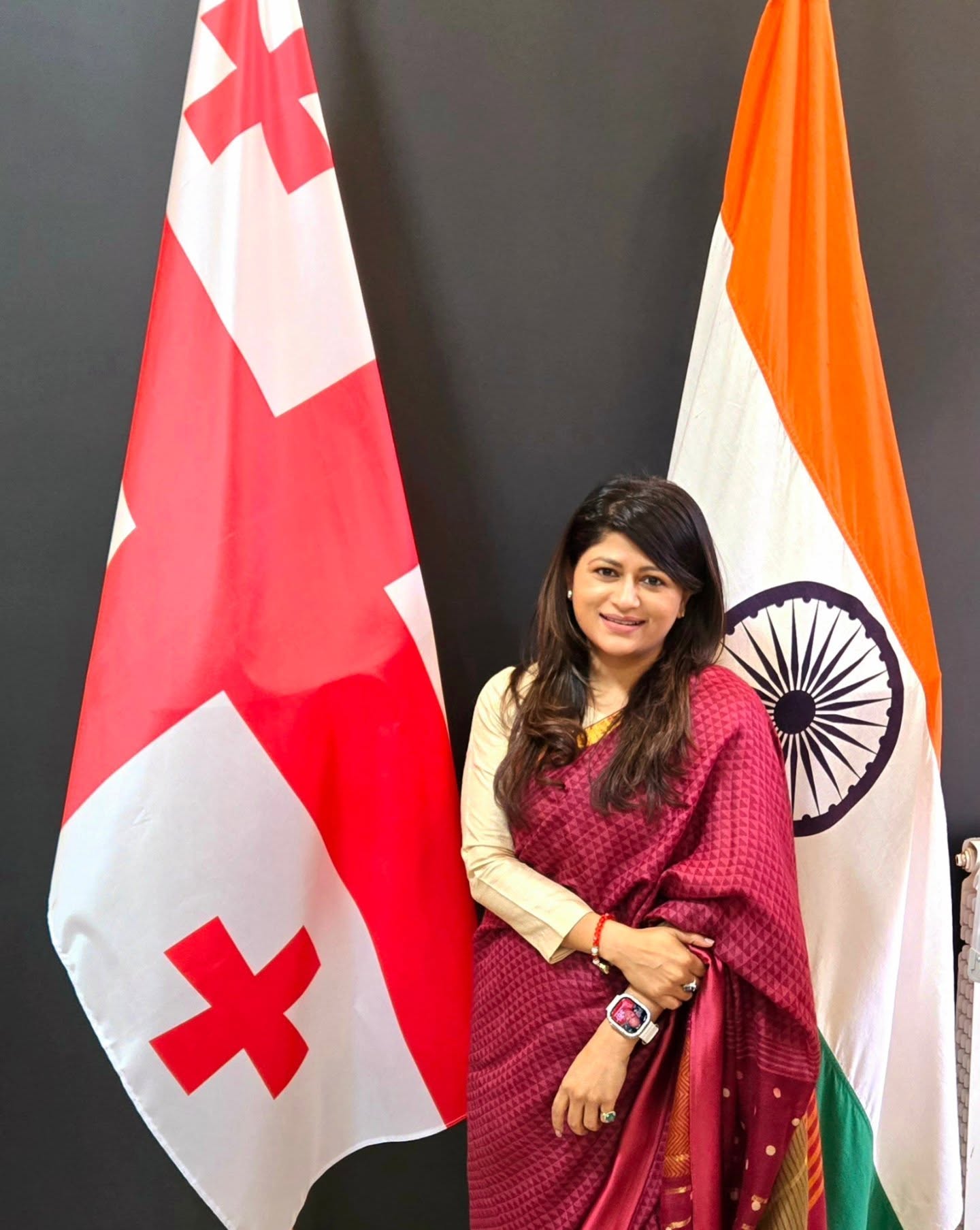 Parul Mahajan in a maroon saree between the Georgian and Indian flags